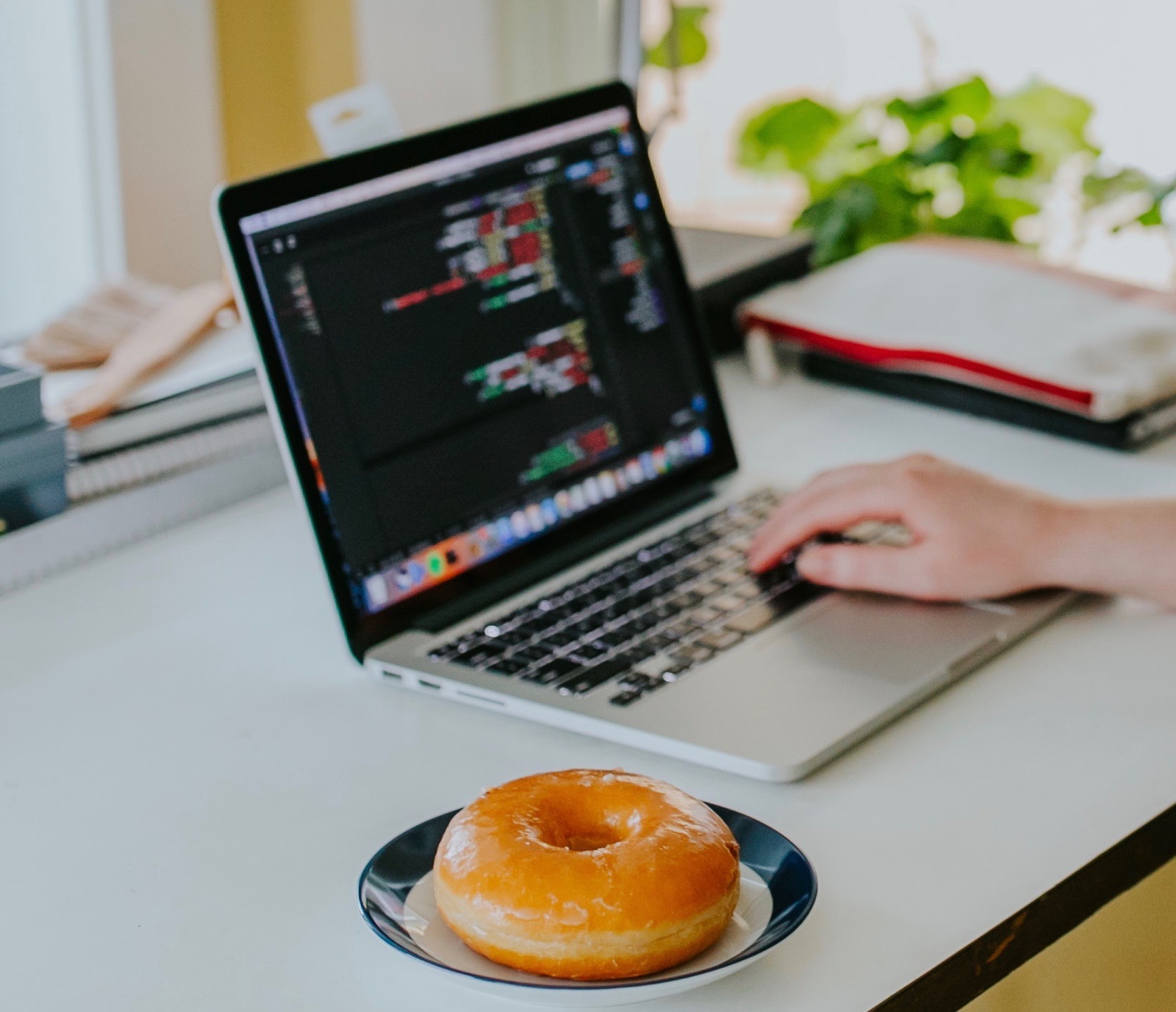 computer with code on the screen and a glazed donut on a white desk